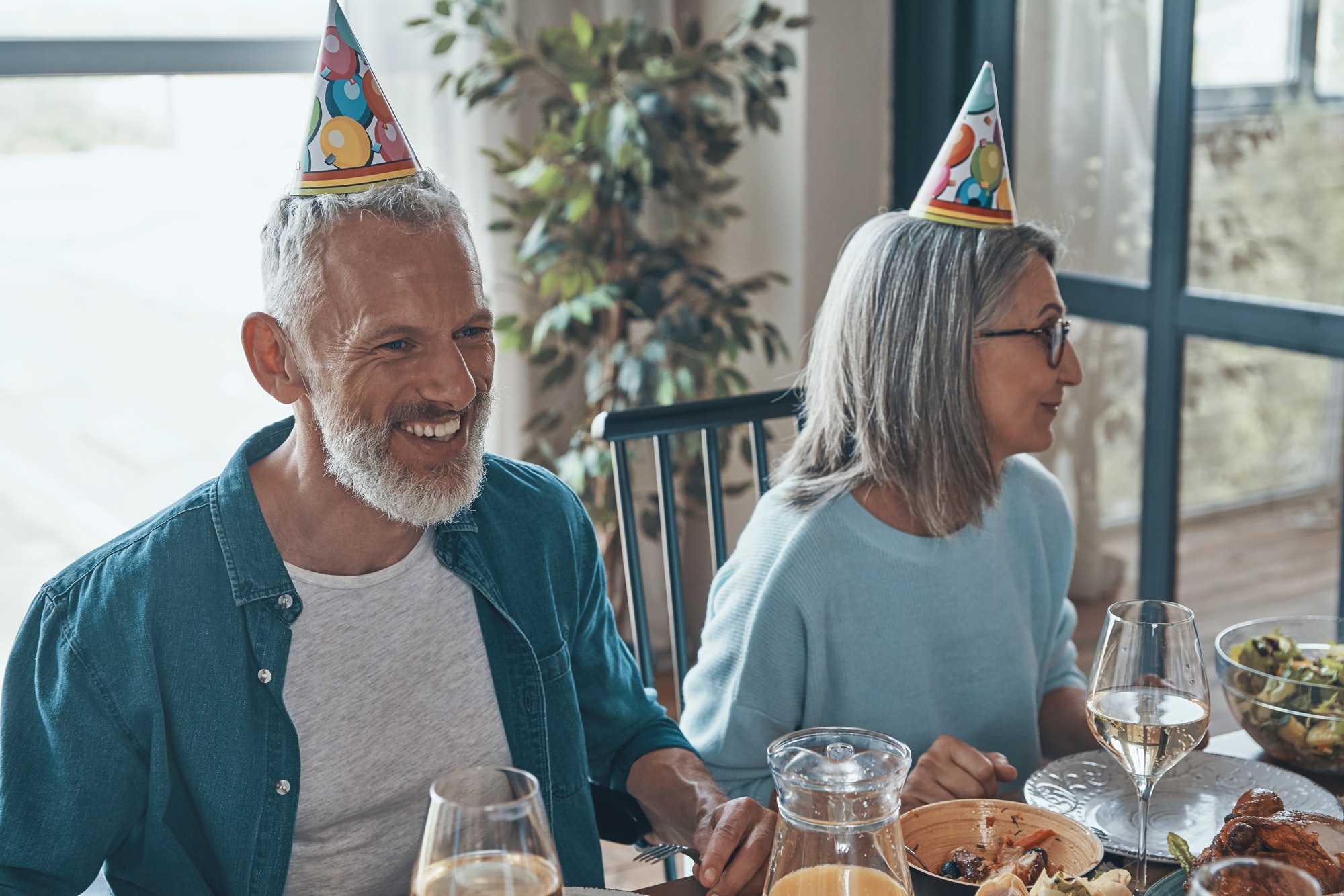 Happy senior couple in funky hats celebrating birthday while sitting at the dining table at home after enrolling in Medicare Part D in the state of Missouri